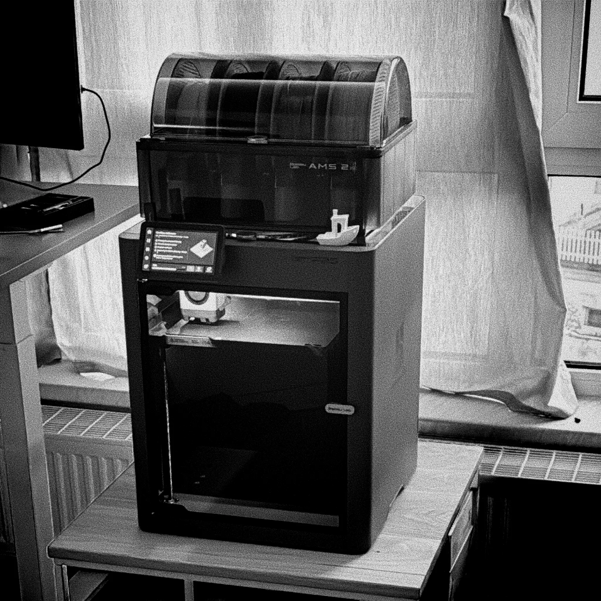 Desktop 3D printer in a home workspace next to a window
